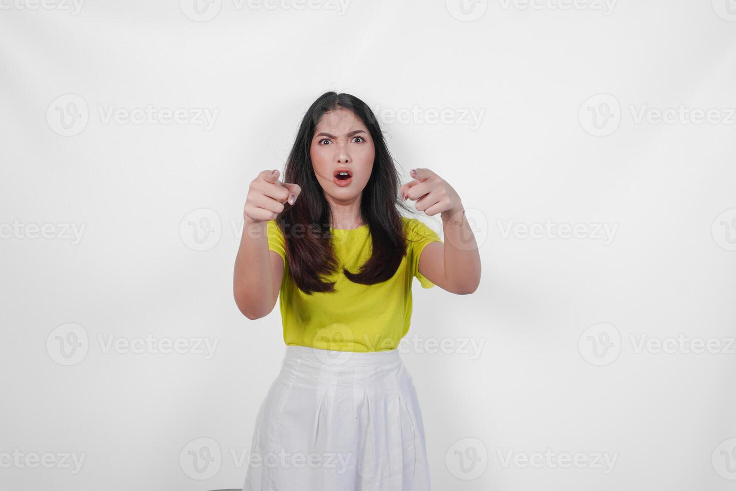 Surprised woman in a yellow shirt pointing to the front with mad expression on her face, isolated by white background. photo