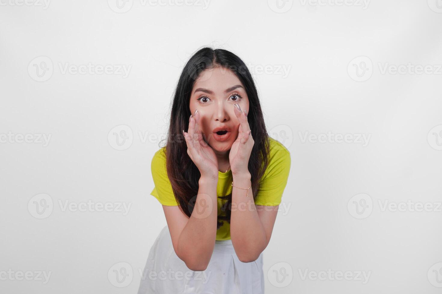 Young Asian woman in a yellow shirt is making a whispering gesture with hands on her face, isolated by white background. Concept of surprise or shock. photo