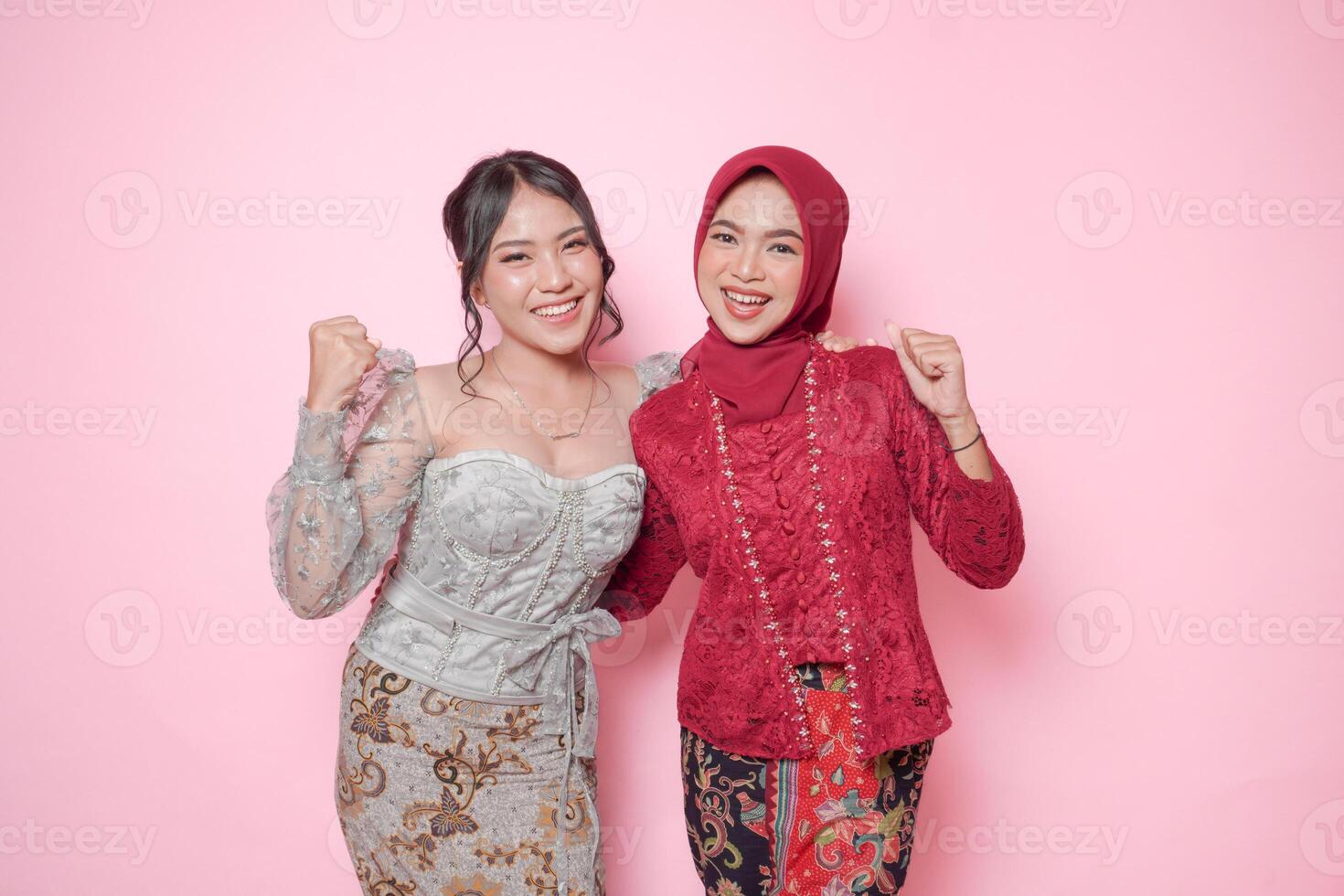 Two excited Asian women wearing modern kebaya dress with a happy successful expression, isolated by pink background. photo