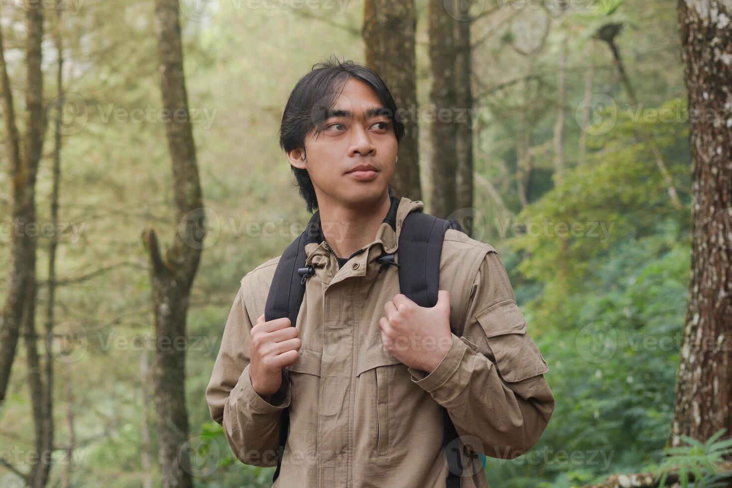Portrait of excited Asian hiker man trekking and hiking in forest nature, wearing backpack and jacket for outdoor camping. Mountain travel concept photo