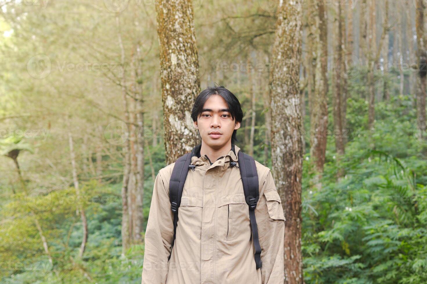 Portrait of excited Asian hiker man trekking and hiking in forest nature, wearing backpack and jacket for outdoor camping. Mountain travel concept photo
