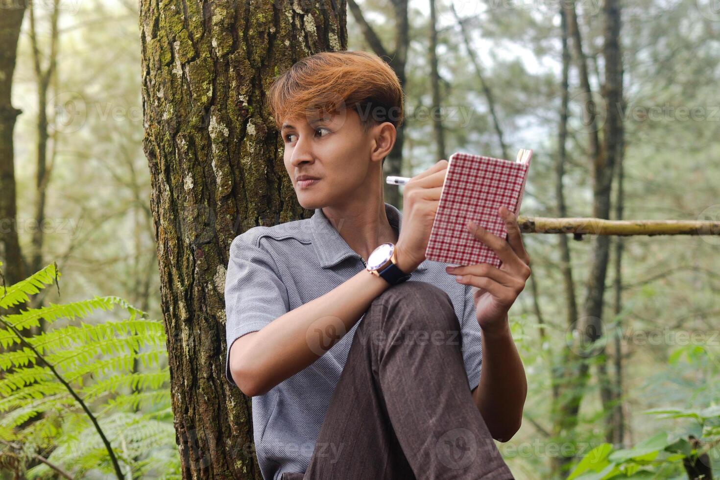 Portrait of confident Asian man writing on notebook while thinking and looking away in the nature forest. Peaceful and relaxing healthcare wellness photo