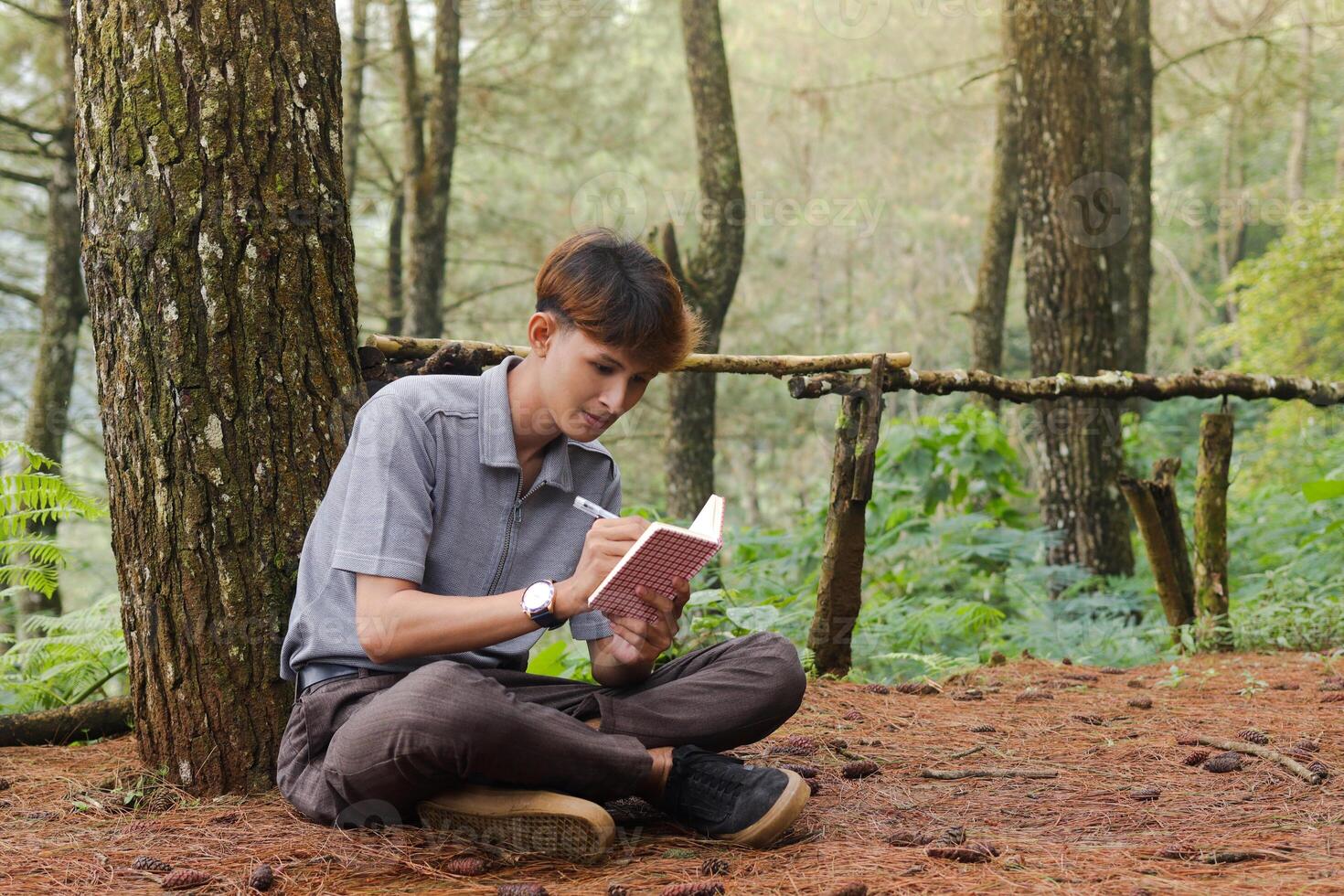 Portrait of confident Asian man writing on notebook while thinking and looking away in the nature forest. Peaceful and relaxing healthcare wellness photo