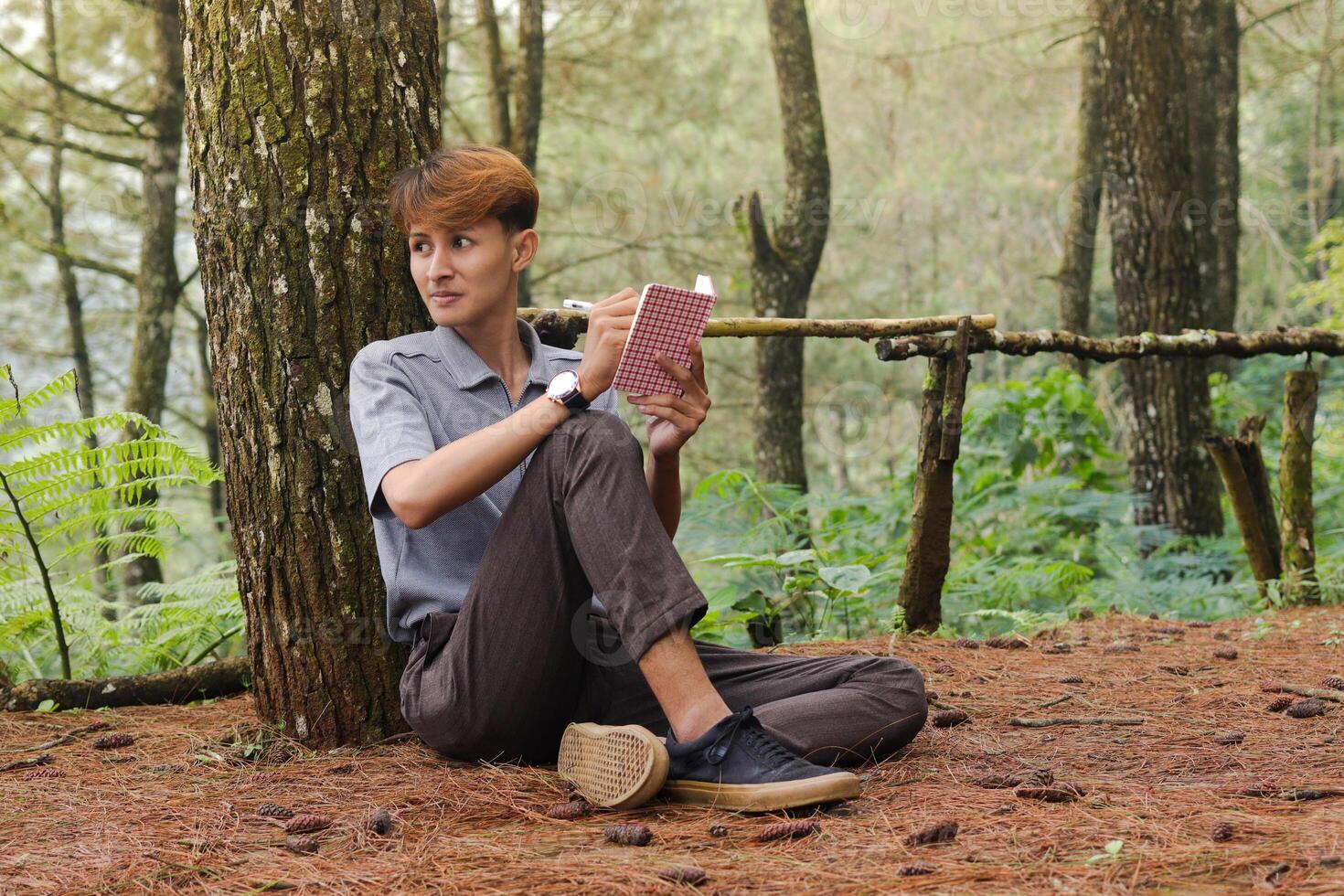 Portrait of confident Asian man writing on notebook while thinking and looking away in the nature forest. Peaceful and relaxing healthcare wellness photo