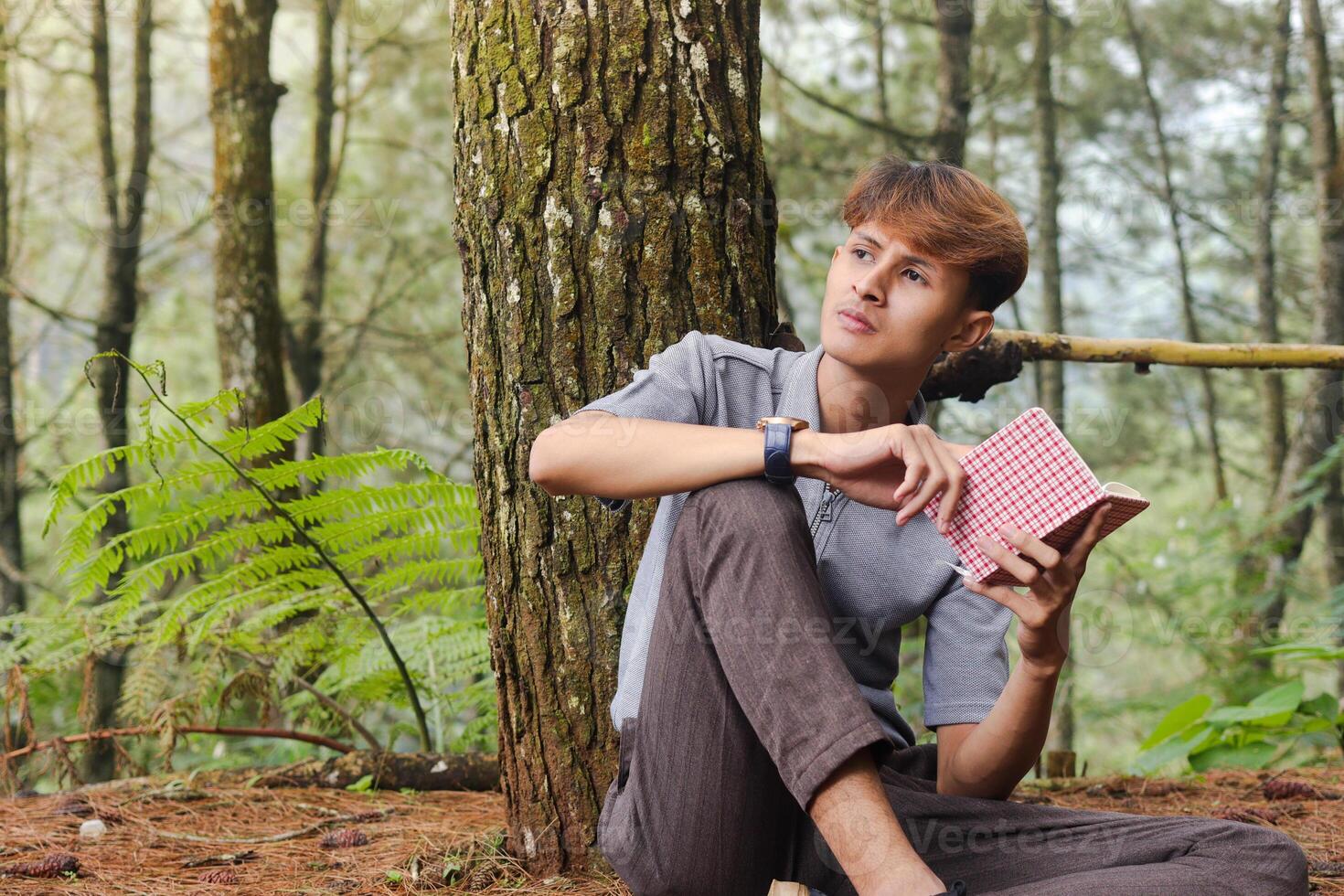 Portrait of confident Asian man writing on notebook while thinking and looking away in the nature forest. Peaceful and relaxing healthcare wellness photo