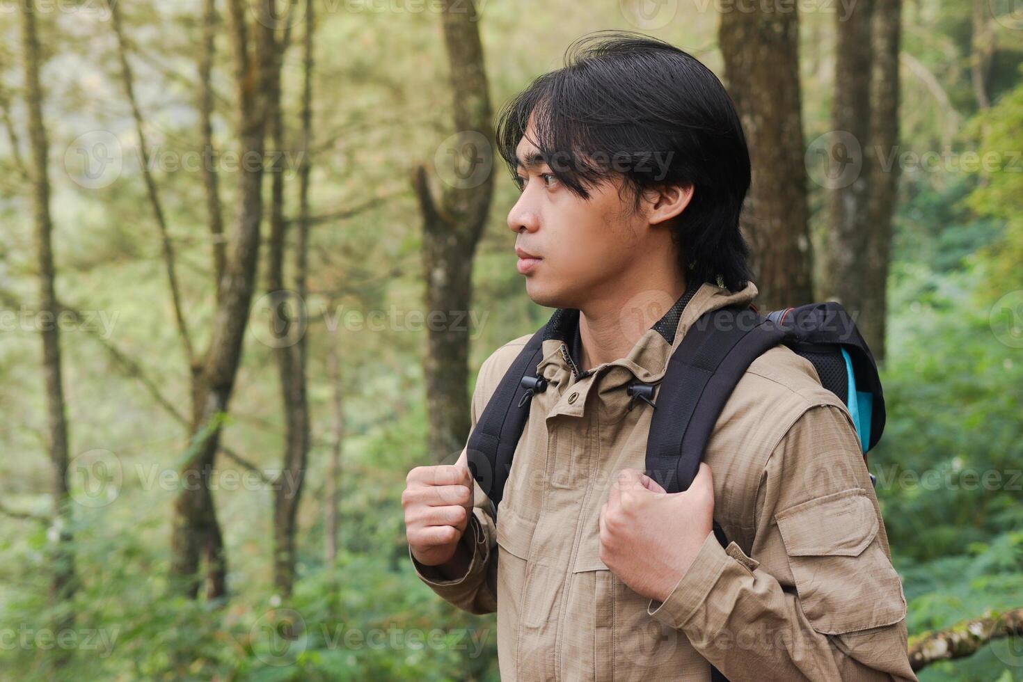 Portrait of excited Asian hiker man trekking and hiking in forest nature, wearing backpack and jacket for outdoor camping. Mountain travel concept photo