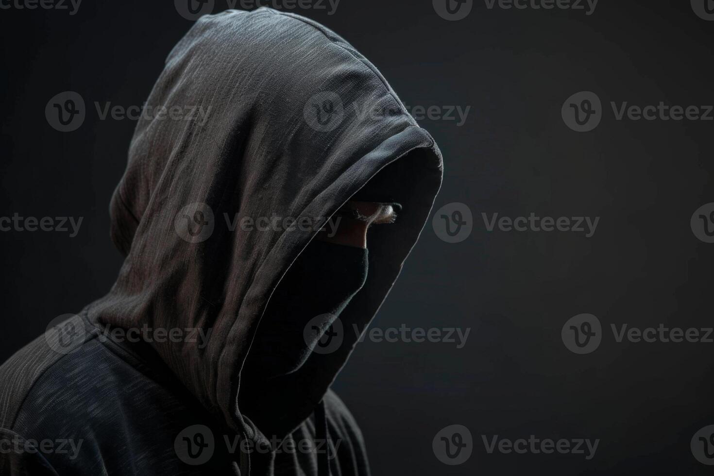 Man in a hood, a shadow hides his face on dark background. Anonymous crime concept photo