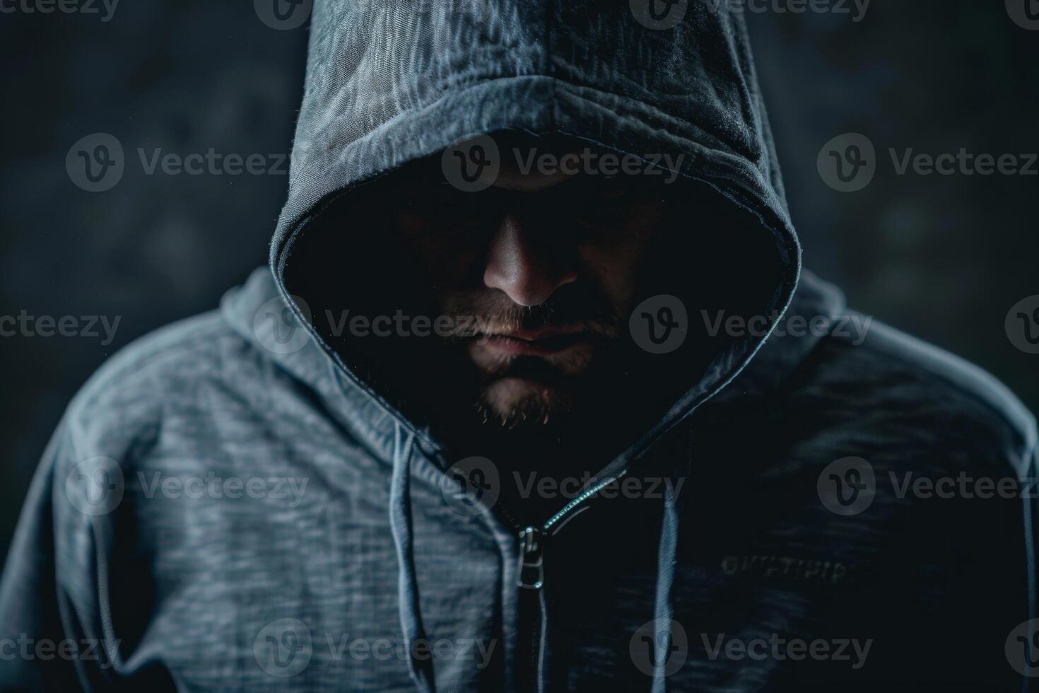 Man in a hood, a shadow hides his face on dark background. Anonymous crime concept photo
