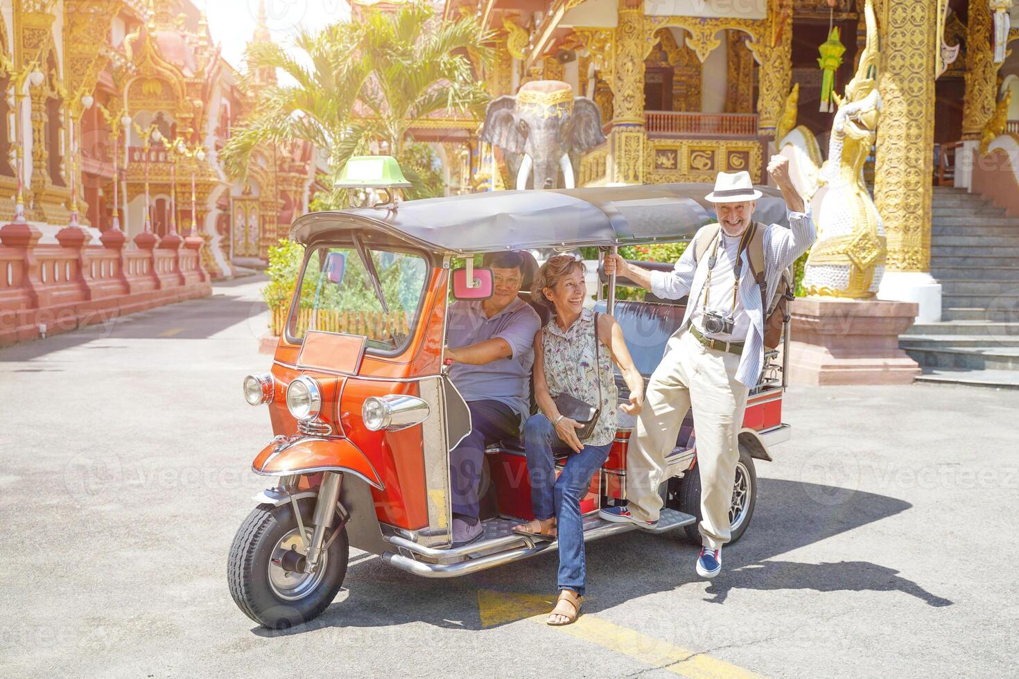 Senior American tourist couple showing funny smiles and laughter while taking photos with Tuk Tuk Thailand taxi in a Thai temple, Chiang Mai city with sun bright background. Senior tourist concept