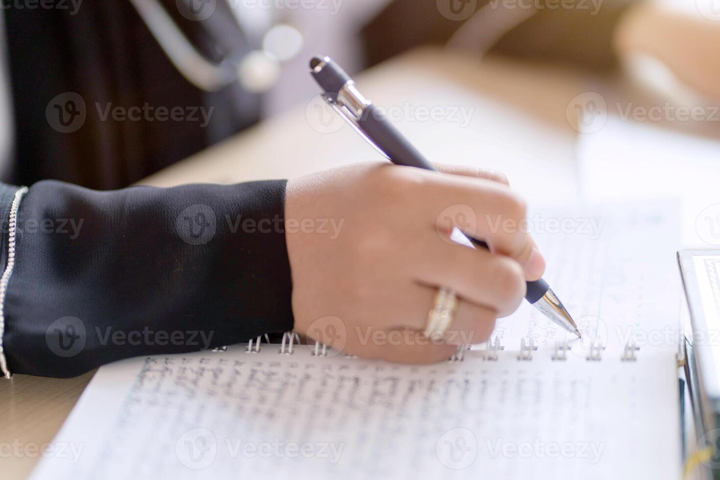Closeup and crop hands of Muslim student in Abaya niqab traditional clothes holding a pen writing on note book in classroom. photo