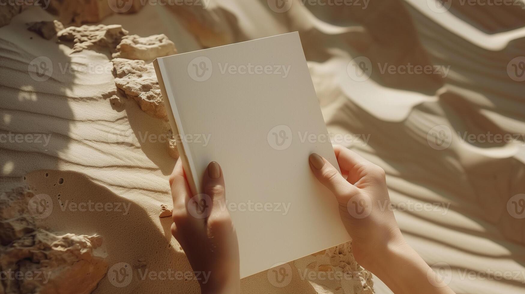 Female hands hold blank notebook mockup on textured sandy surface. Sunlight casts soft shadows. Journal template advertising image. Book cover mock up product photorealistic photo