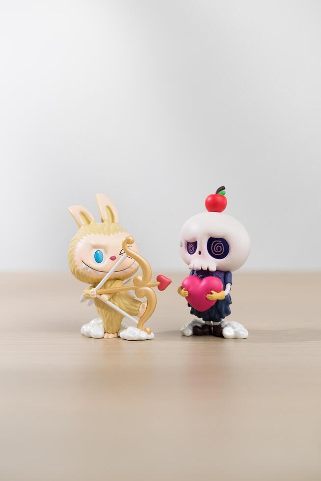 Labubu and Tycoco the monsters mischief diary, Two whimsical figures, a rabbit with a bow and a skull-headed figure holding an apple, engage in a playful interaction. photo