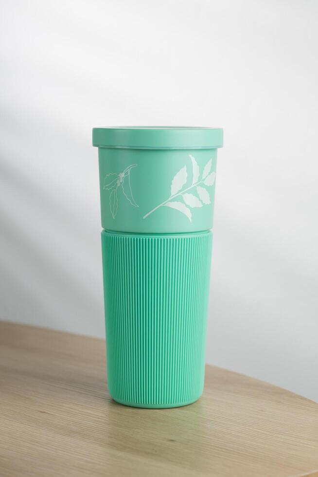 A mint green tumbler stands on a wooden surface, its ribbed texture and leaf design suggesting an eco-friendly alternative to disposable cups. photo