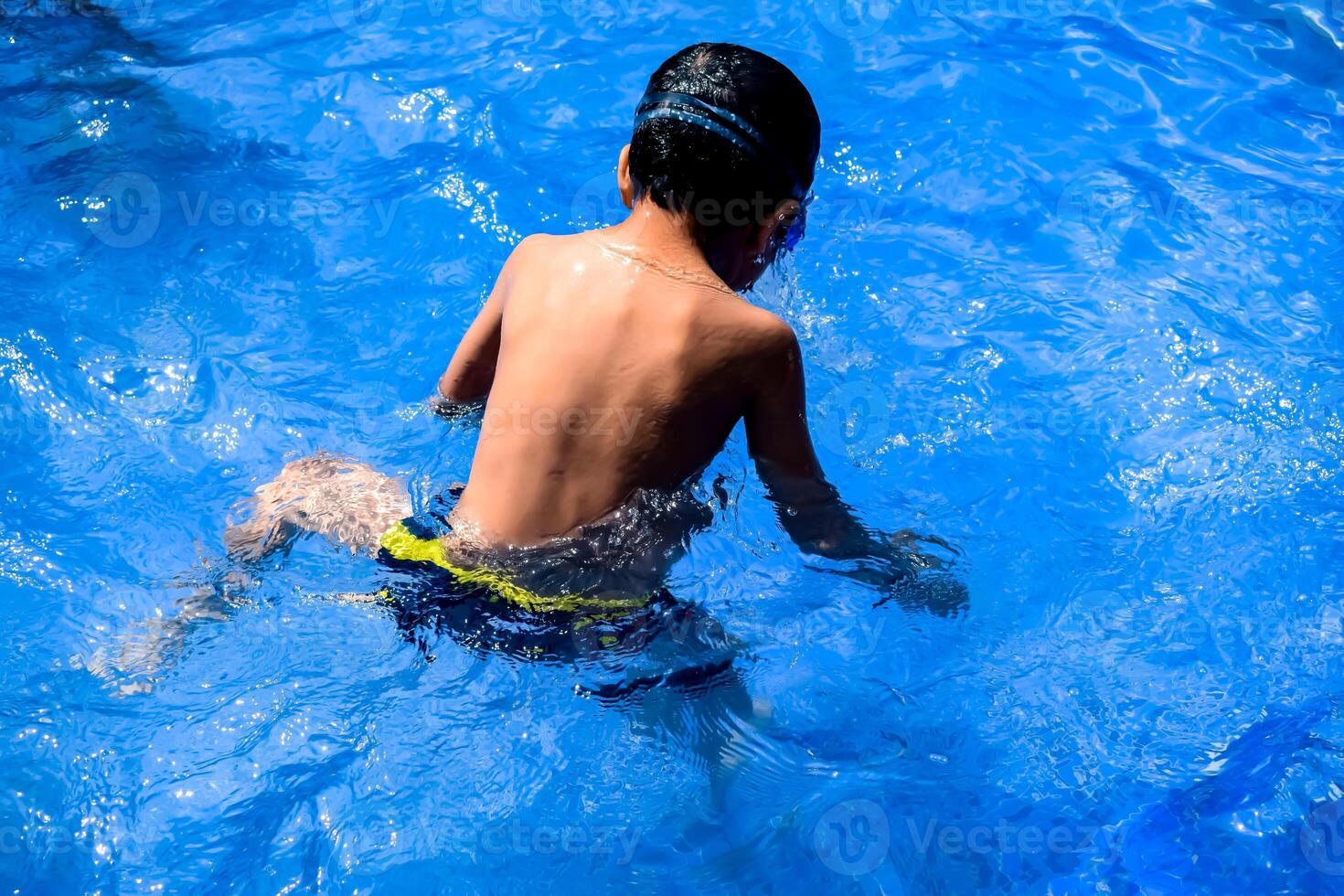 Happy Indian boy swimming in a pool, Kid wearing swimming costume along with air tube during hot summer vacations, Children boy in big swimming pool. photo