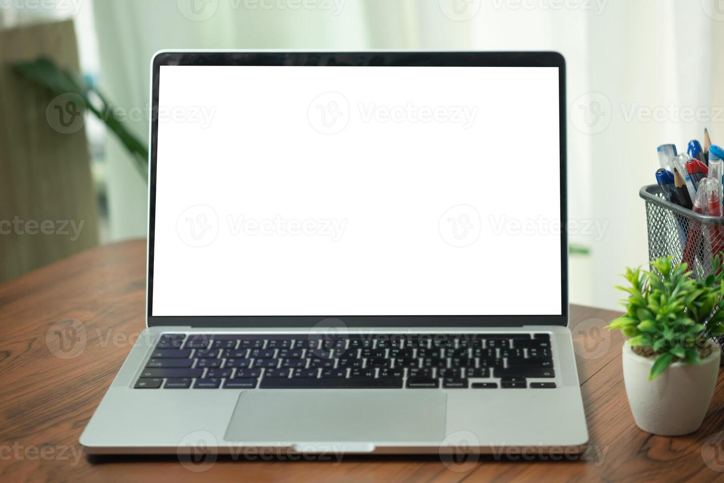 Open laptop with a blank white screen on a wooden desk with potted plant and pen holder, representing a clean and organized workspace. photo