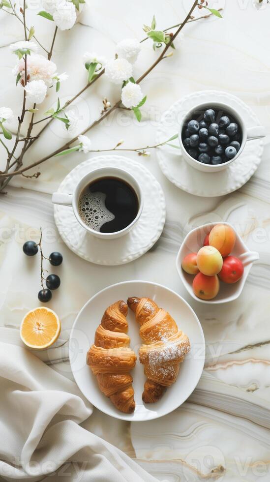 Early breakfast with black strong aromatic coffee and a croissant, complemented by fresh berries and flowers in white dishes photo
