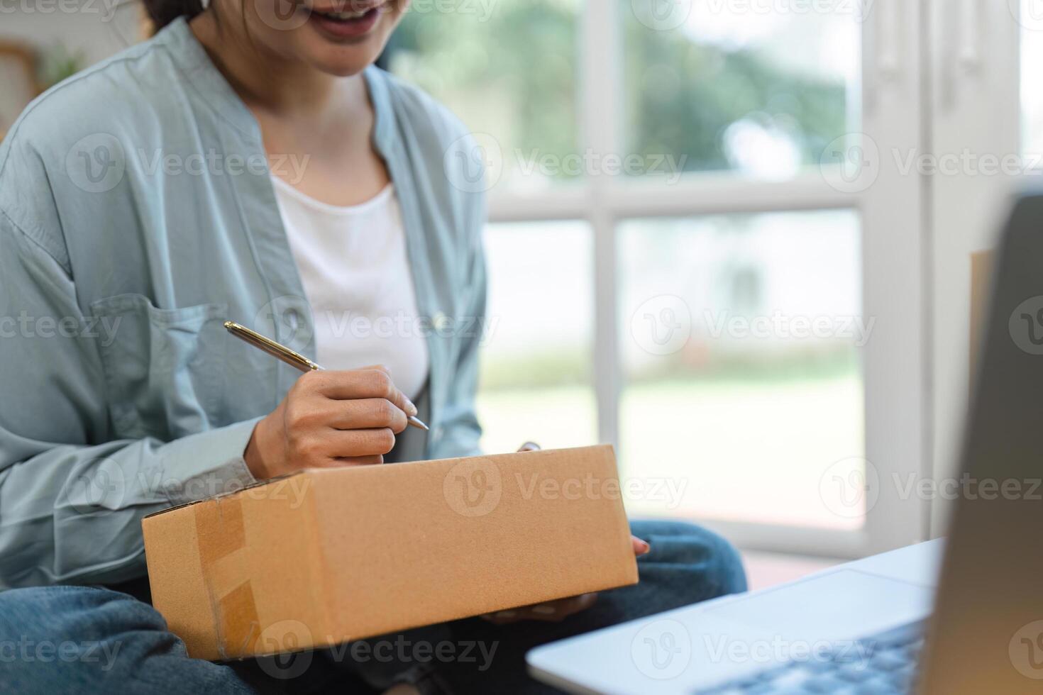 Young Woman Managing Her Small Online Sales Business from Home, Writing on a Package, Preparing for Shipment photo