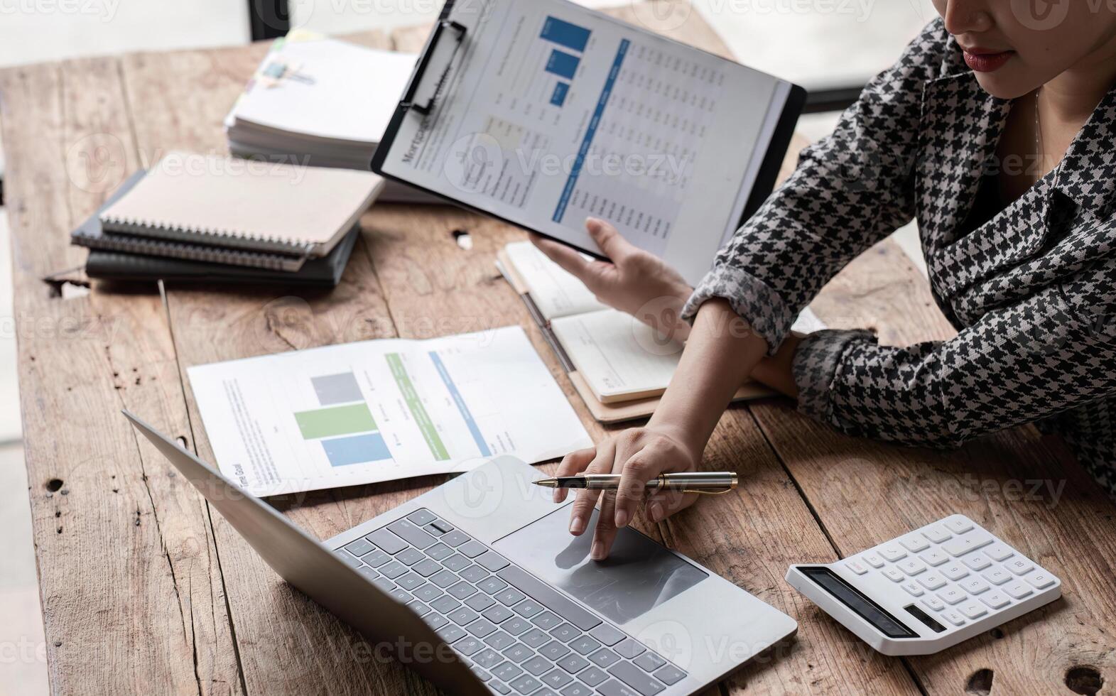 Young Accountant Analyzing Financial Documents and Data on Laptop at Wooden Desk in Modern Office Environment photo