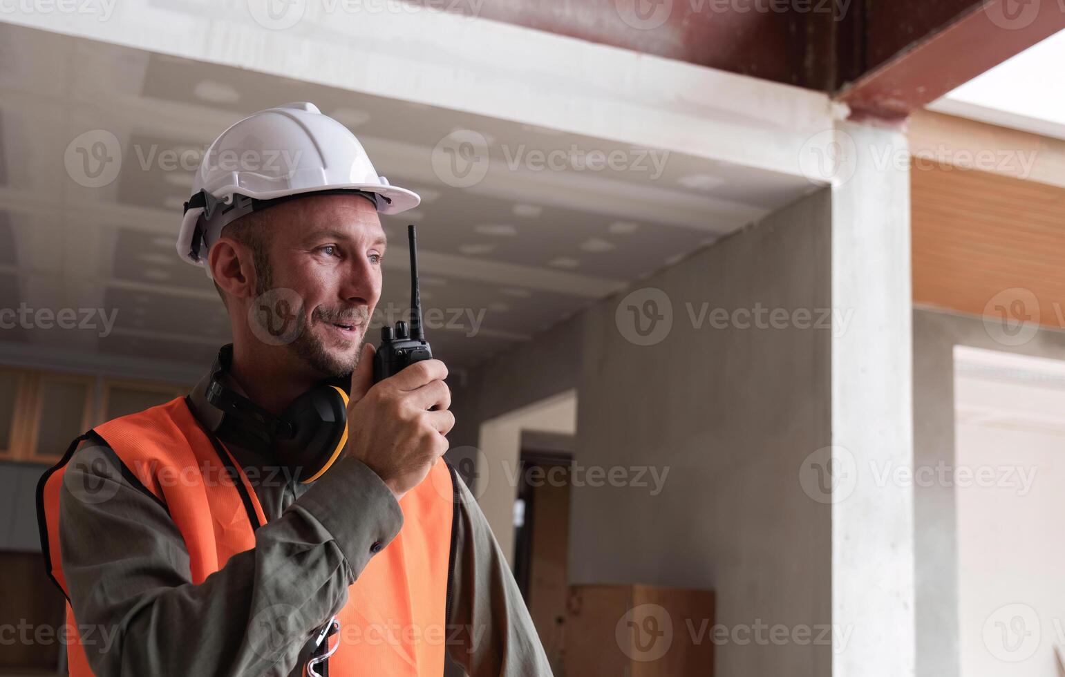 Young Engineer Communicating on Construction Site with Walkie-Talkie, Wearing Safety Gear and Helmet, Overseeing Modern Building Project photo