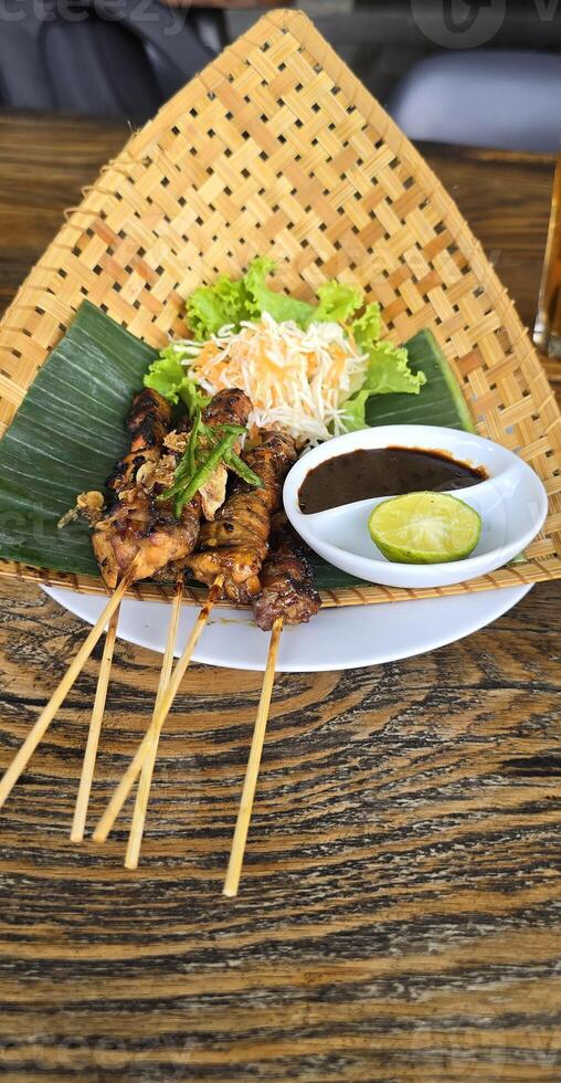 Chicken grilled satay skewers served with lime and peanut sauce on black, top view. Asian thai style food. photo