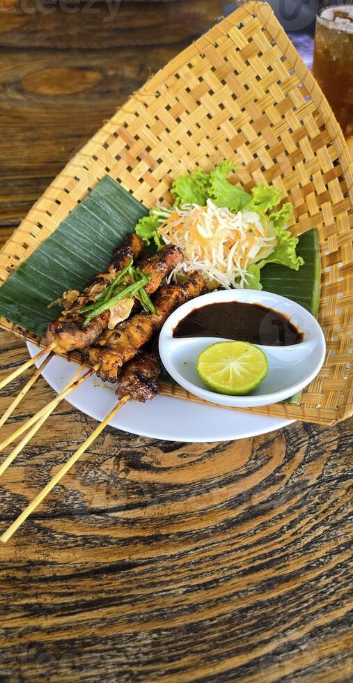 Chicken grilled satay skewers served with lime and peanut sauce on black, top view. Asian thai style food. photo