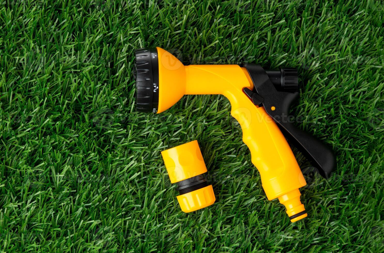 yellow nozzle on a hose for watering lying on a grass photo