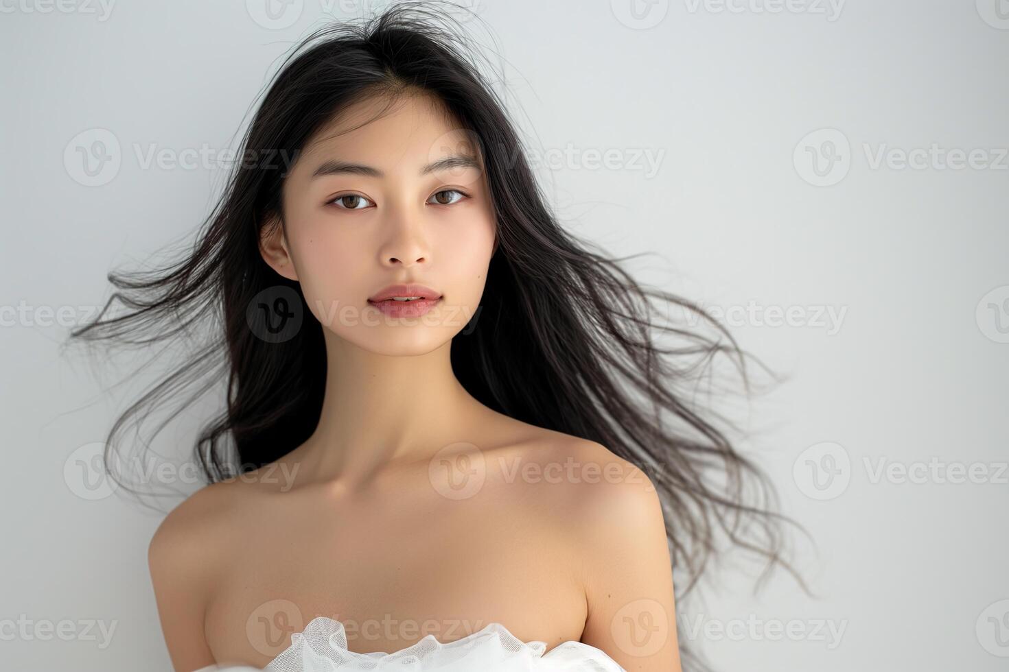 A beautiful young Asian woman with long hair and a white strapless dress is isolated against a plain background photo