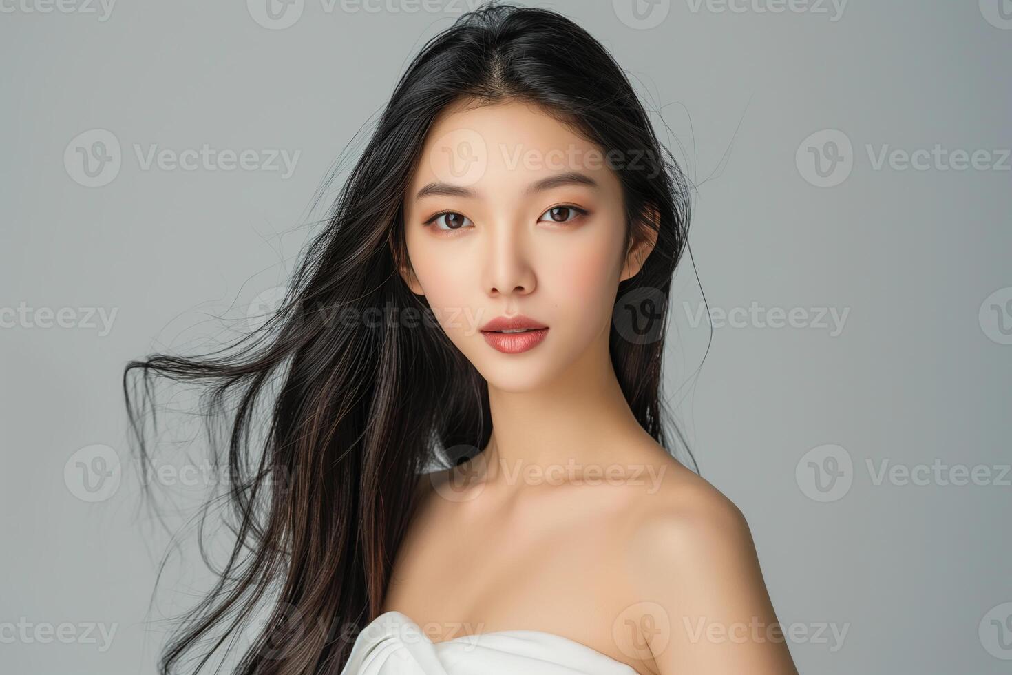 A beautiful young Asian woman with long hair and a white strapless dress is isolated against a plain background photo