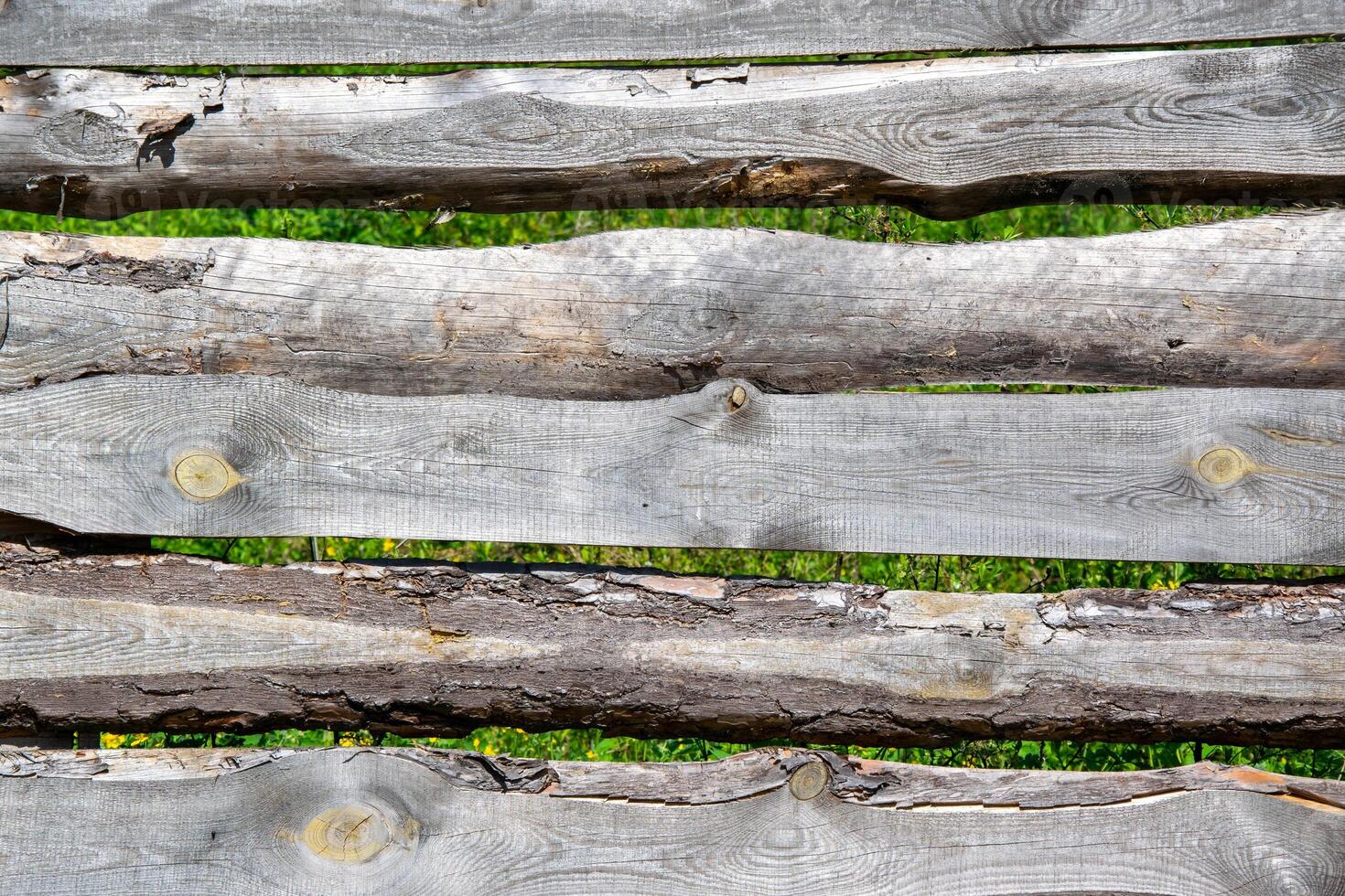 Close-up of a rustic wooden fence with natural textures and green foliage peeking through the gaps photo