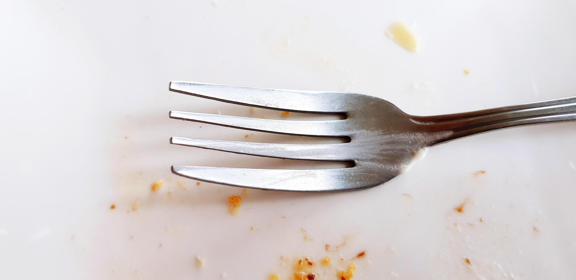 Close up stainless steel fork on dirty white plate or dish after eating dessert or food. Single object concept. photo