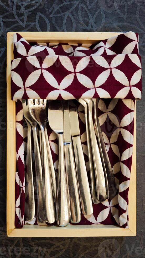 Top View of Silver Cutlery Set in Wooden Box with Patterned Fabric Lining on Textured Surface photo
