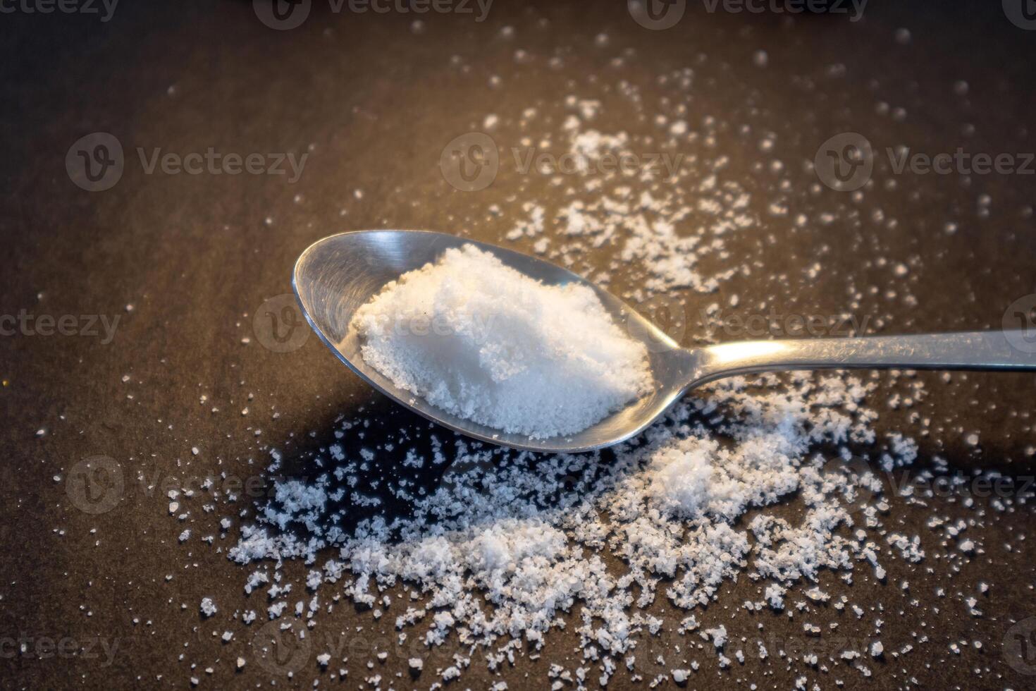 Ground sea salt or salt crystals powder on the spoon with dark background photo