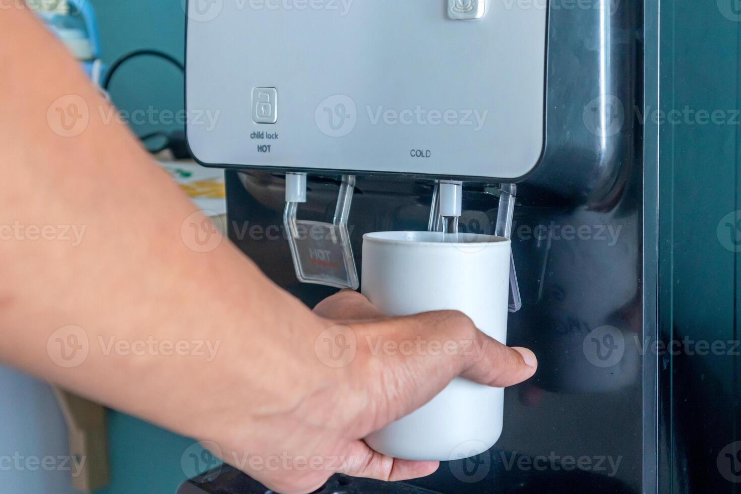 A male hand filling a cup with water from water cooler or water dispenser photo