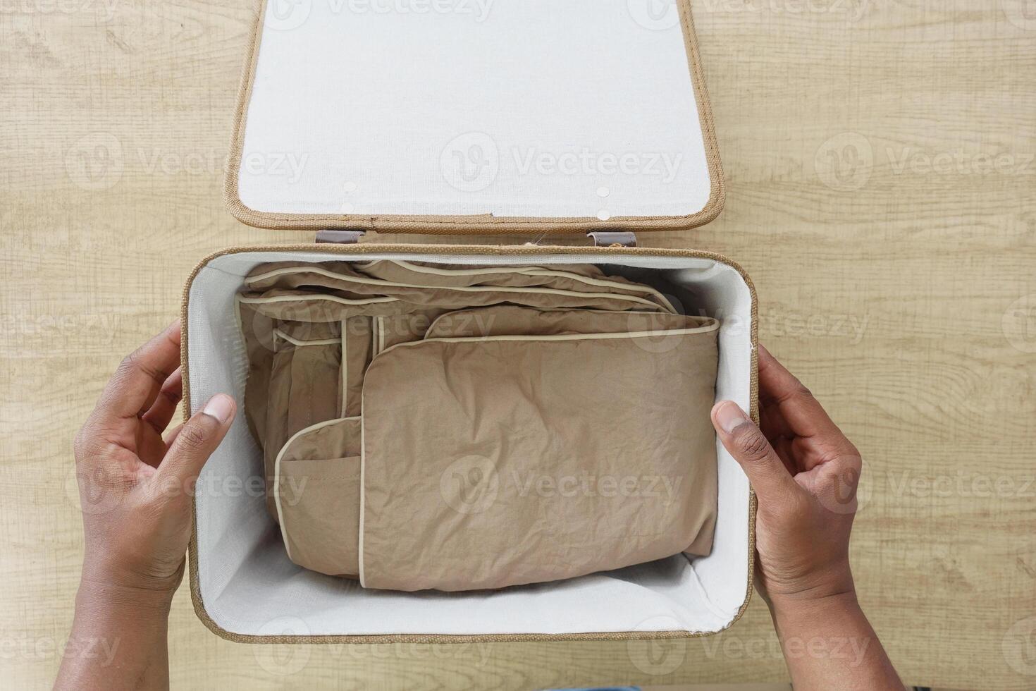 Someone is meticulously organizing garments in a storage container on a table made of wood photo