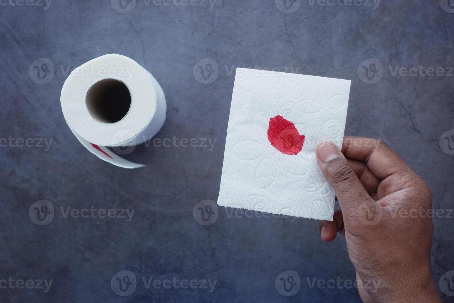 A blood spot is noticeable on a tissue next to a roll of toilet paper in the background photo