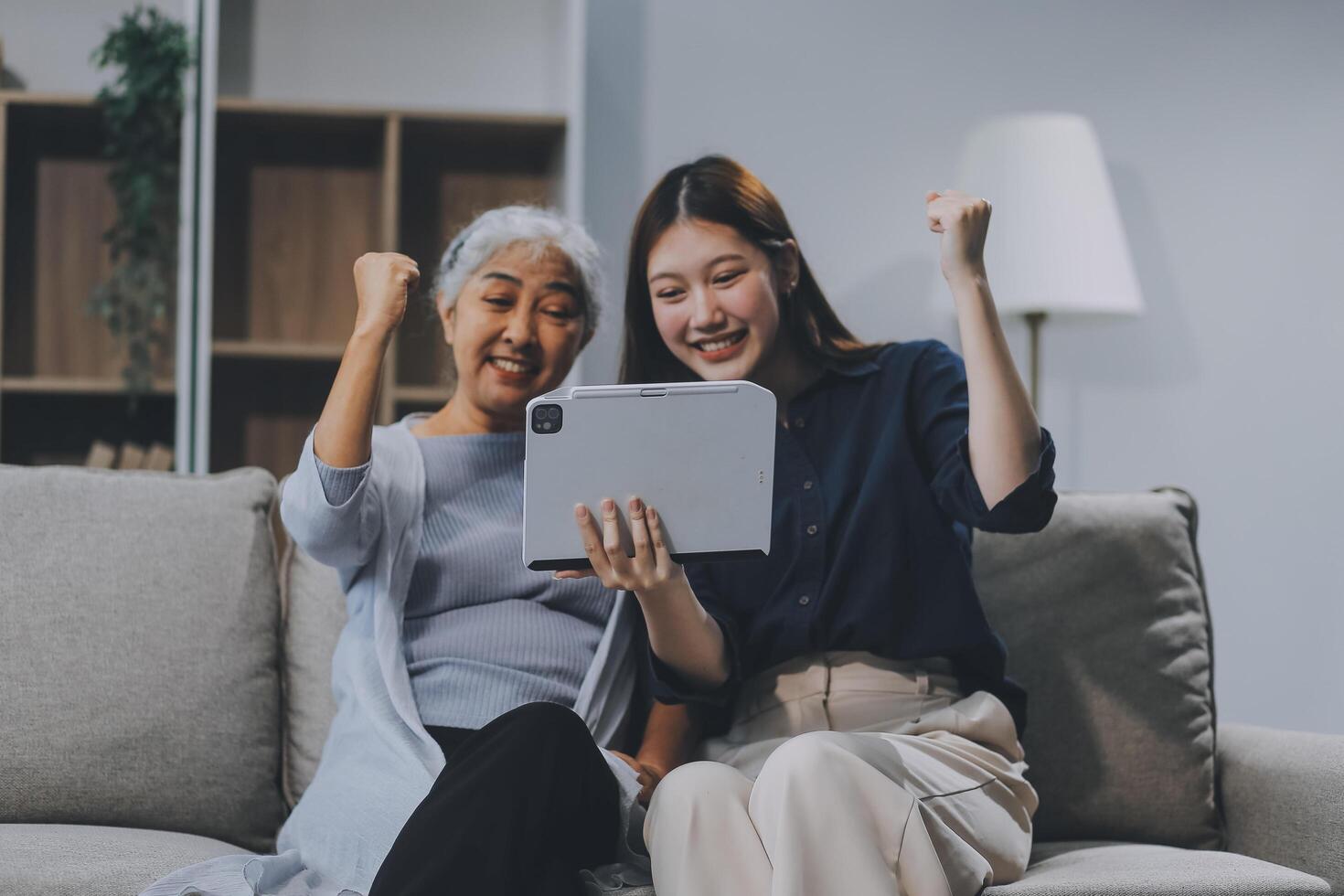 Happy grownup daughter showing content on tablet to mature mother. Two family generations women with digital computer gadget resting on couch together, watching videos, making call photo