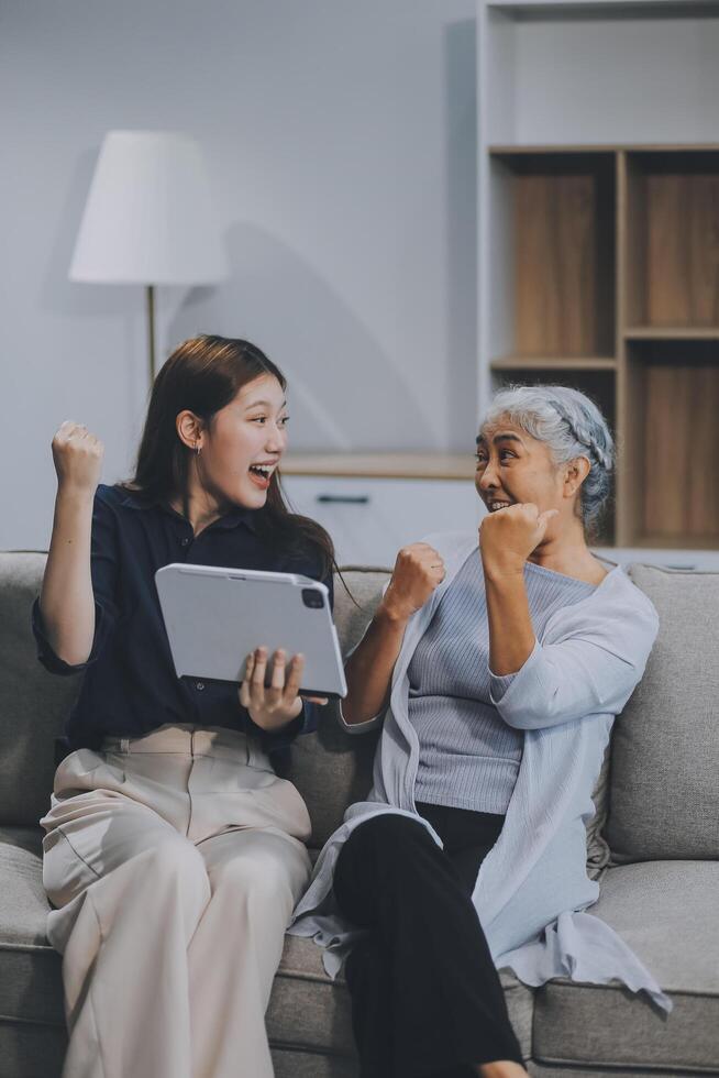 Happy grownup daughter showing content on tablet to mature mother. Two family generations women with digital computer gadget resting on couch together, watching videos, making call photo