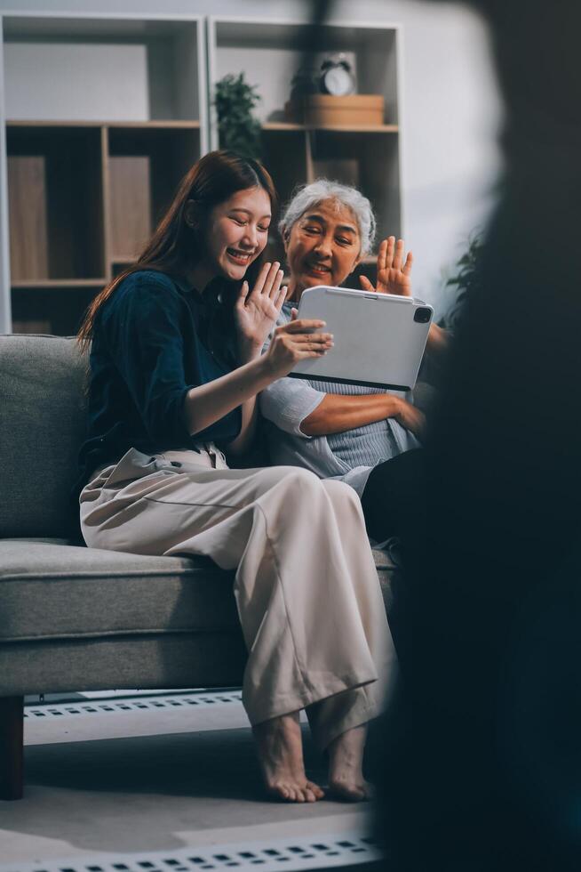Happy grownup daughter showing content on tablet to mature mother. Two family generations women with digital computer gadget resting on couch together, watching videos, making call photo