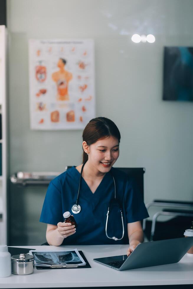 Female doctor writing in a notebook and holding a medicine bottle works at a computer while there were many medicine bottles on the table while sitting at a work desk photo