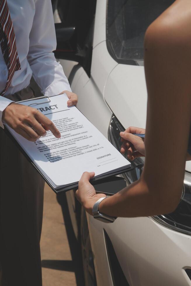 Side view of writing on clipboard while insurance agent examining car after accident photo