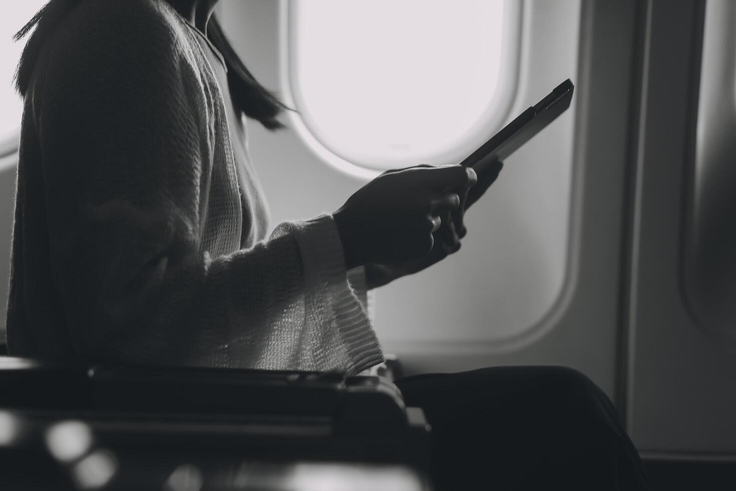 Young asian businesswoman in formal clothes working using tablet with smart pen while sitting in airplane cabin near window traveling to another place photo