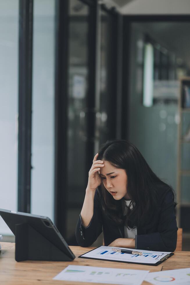 Young sad businesswoman is sitting at table, covering his face On desk is laptop, tablet computer, Stress. Serious woman concentrating on his paper work. photo