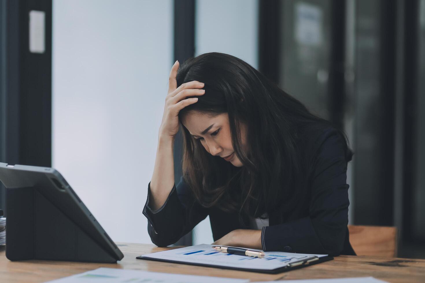 Young sad businesswoman is sitting at table, covering his face On desk is laptop, tablet computer, Stress. Serious woman concentrating on his paper work. photo