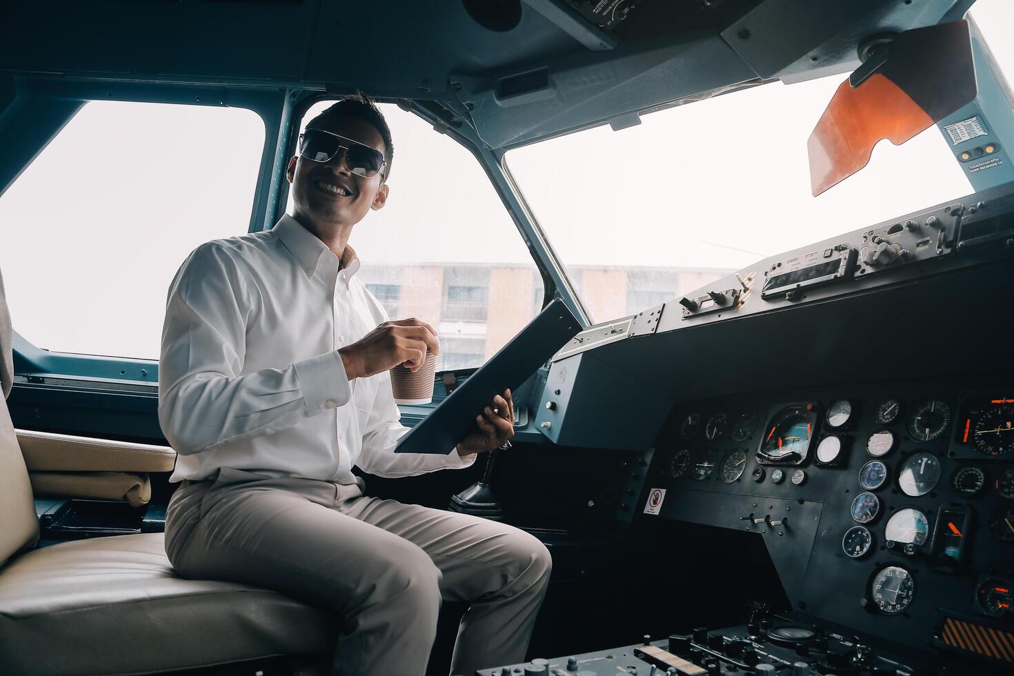 People and occupation concept. Adult captain of jet airliner wearing black leather jacket and headset sitting in front of onboard instruments, filling in safety report before departure. Blurred shot photo
