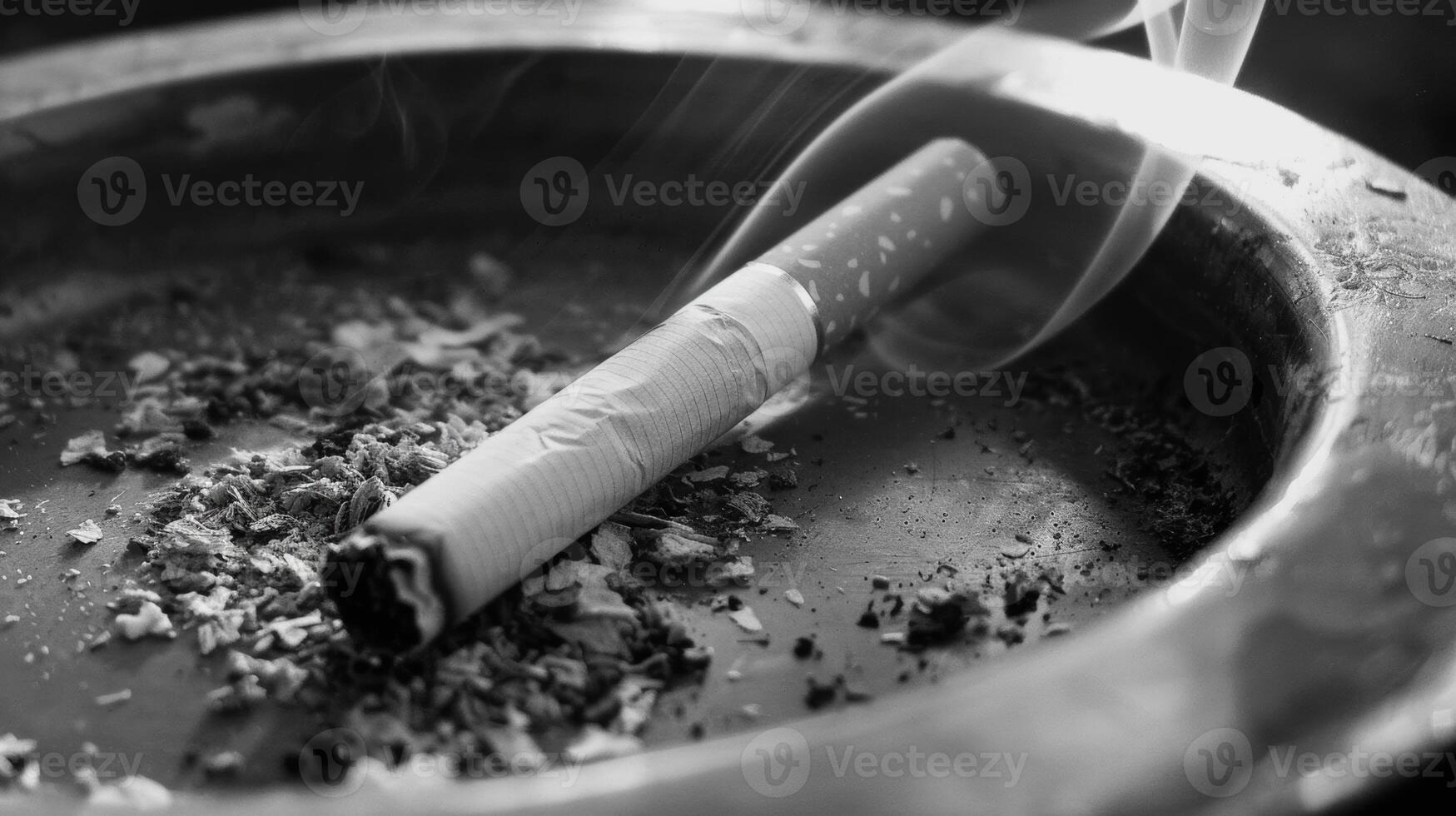 Black and white photo of burning cigarette in ashtray