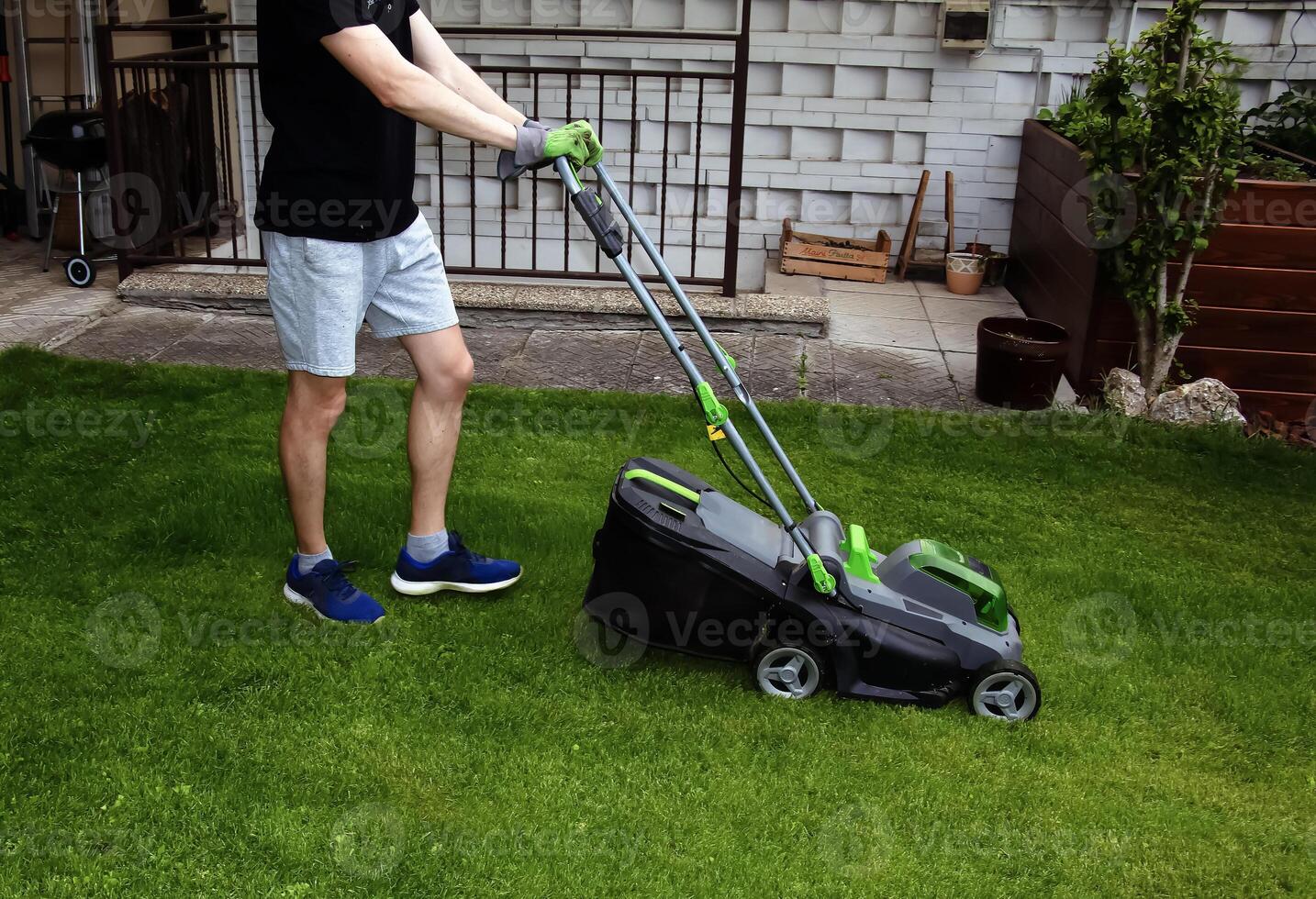 A young man is mowing a lawn with a lawn mower in his beautiful green floral summer garden photo