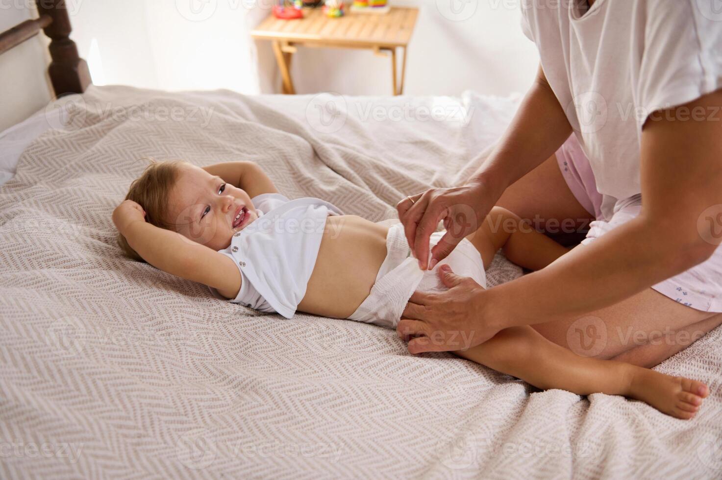 Mother changing diaper of a happy baby on a comfortable bed in a cozy home setting photo