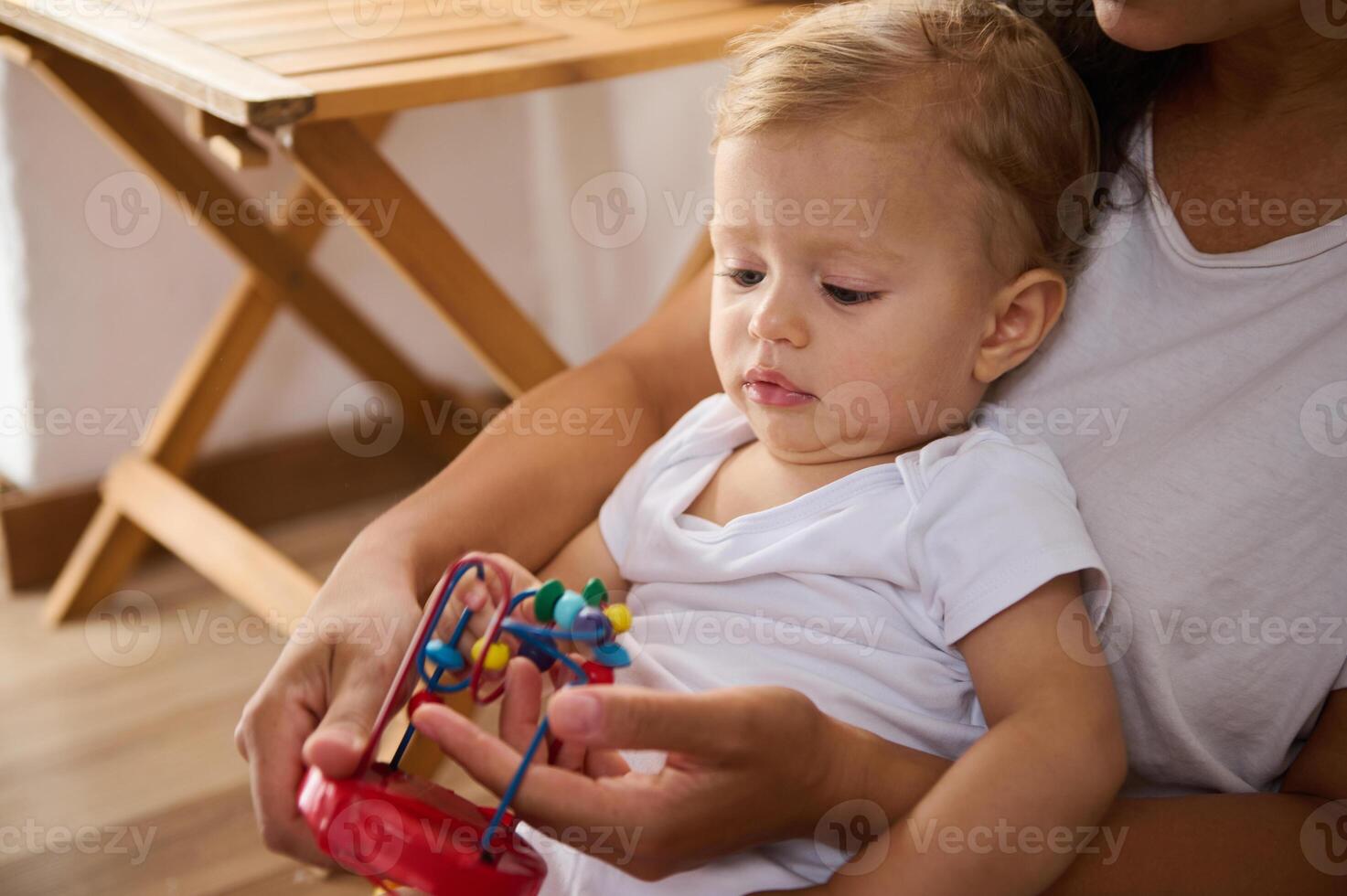 Mother holding baby while he plays with colorful toy at home photo