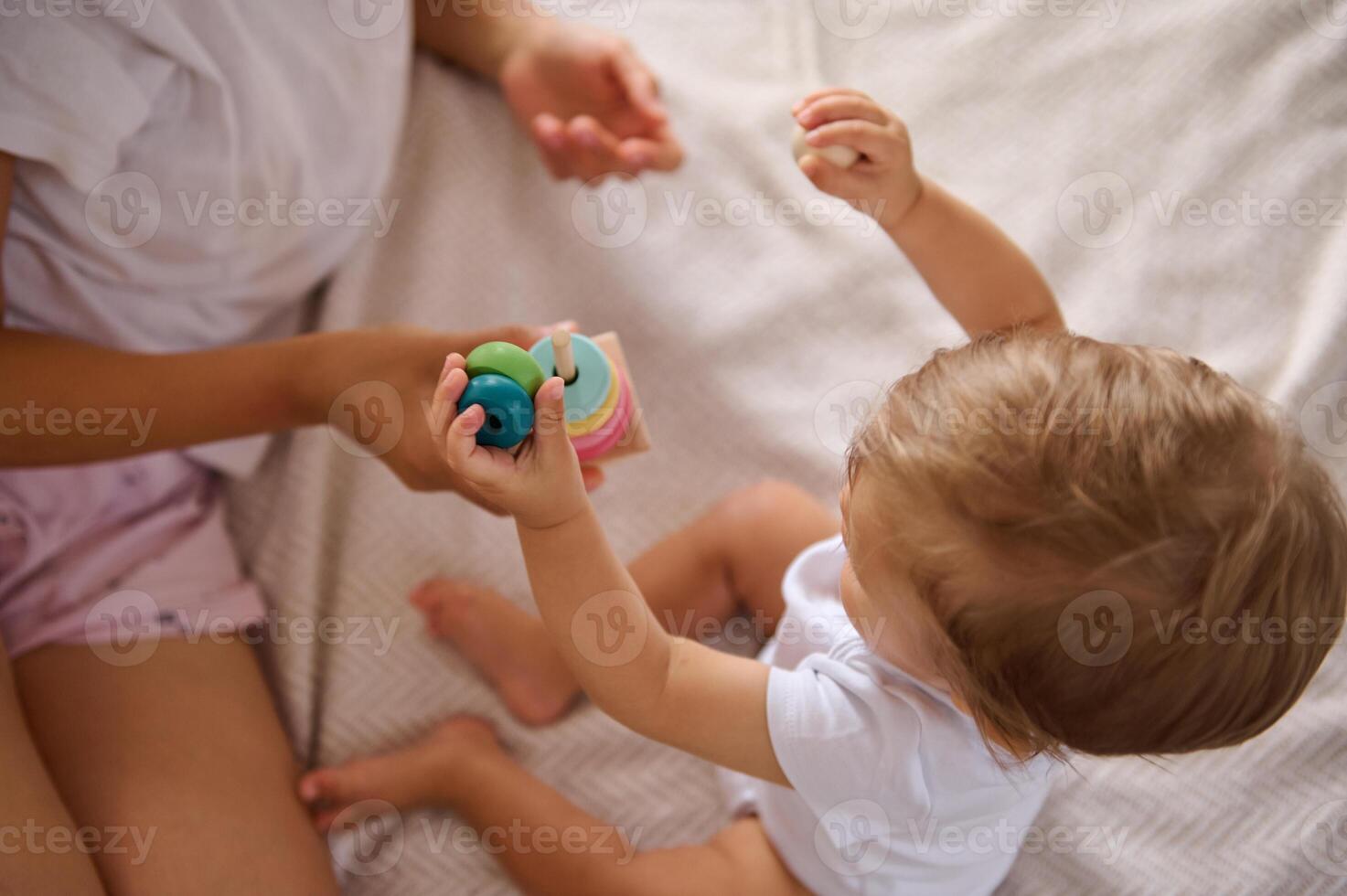 Baby playing with colorful stacking toy blocks with mother on cozy bed photo