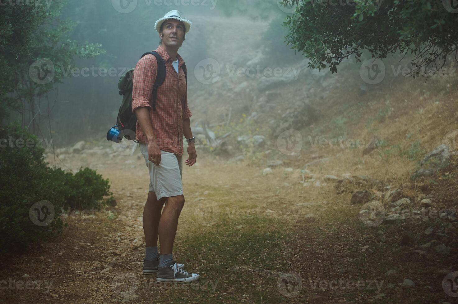 Man hiking in foggy forest path wearing hat and backpack photo